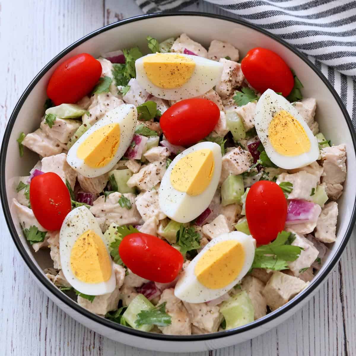 Turkey salad with eggs and tomatoes in a white bowl.