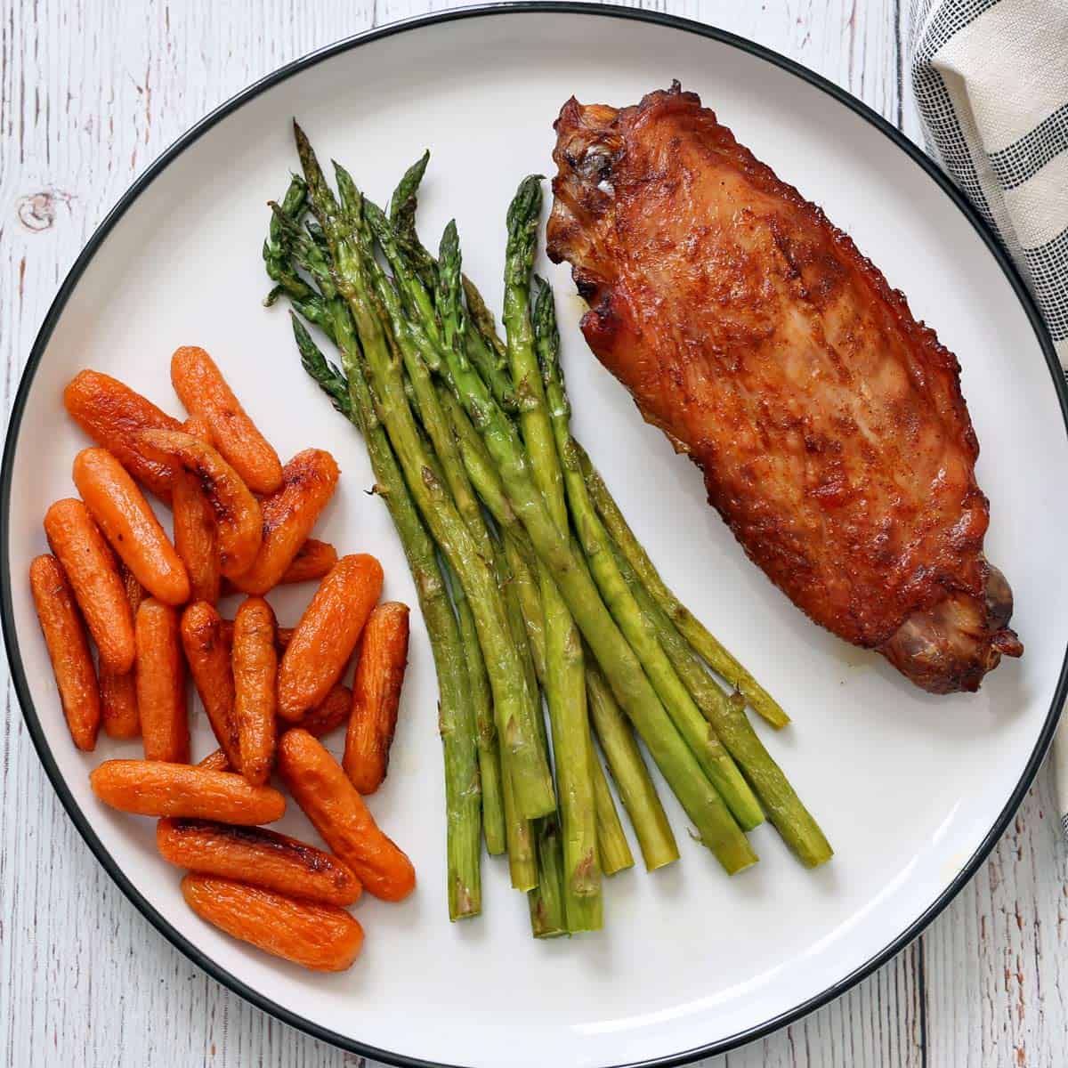 Roasted carrots and asparagus are served as side dishes for a turkey wing.