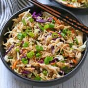 Chinese chicken salad is served in a dark bowl with chopsticks.