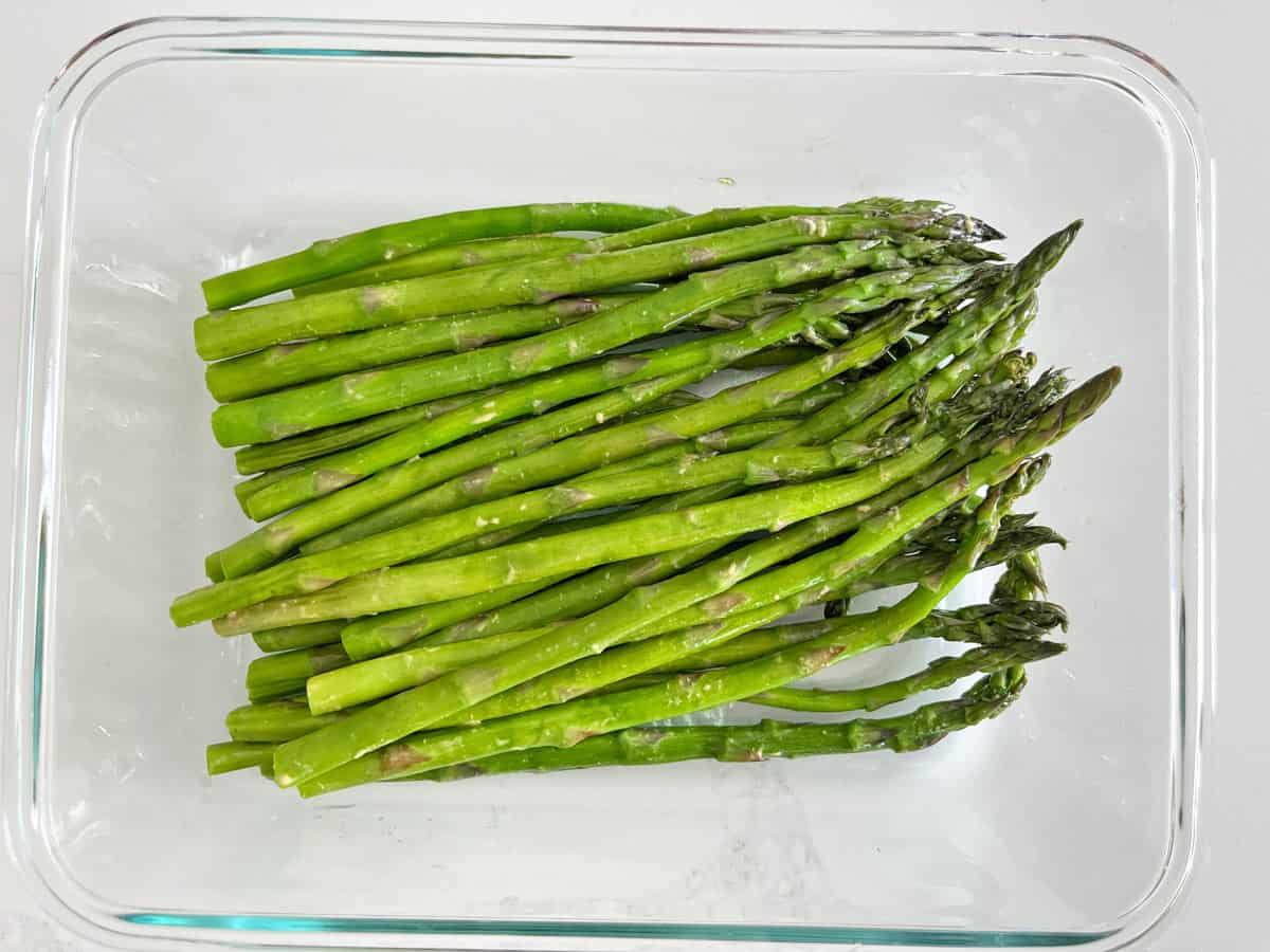 Microwave asparagus is stored in a glass food storage container.