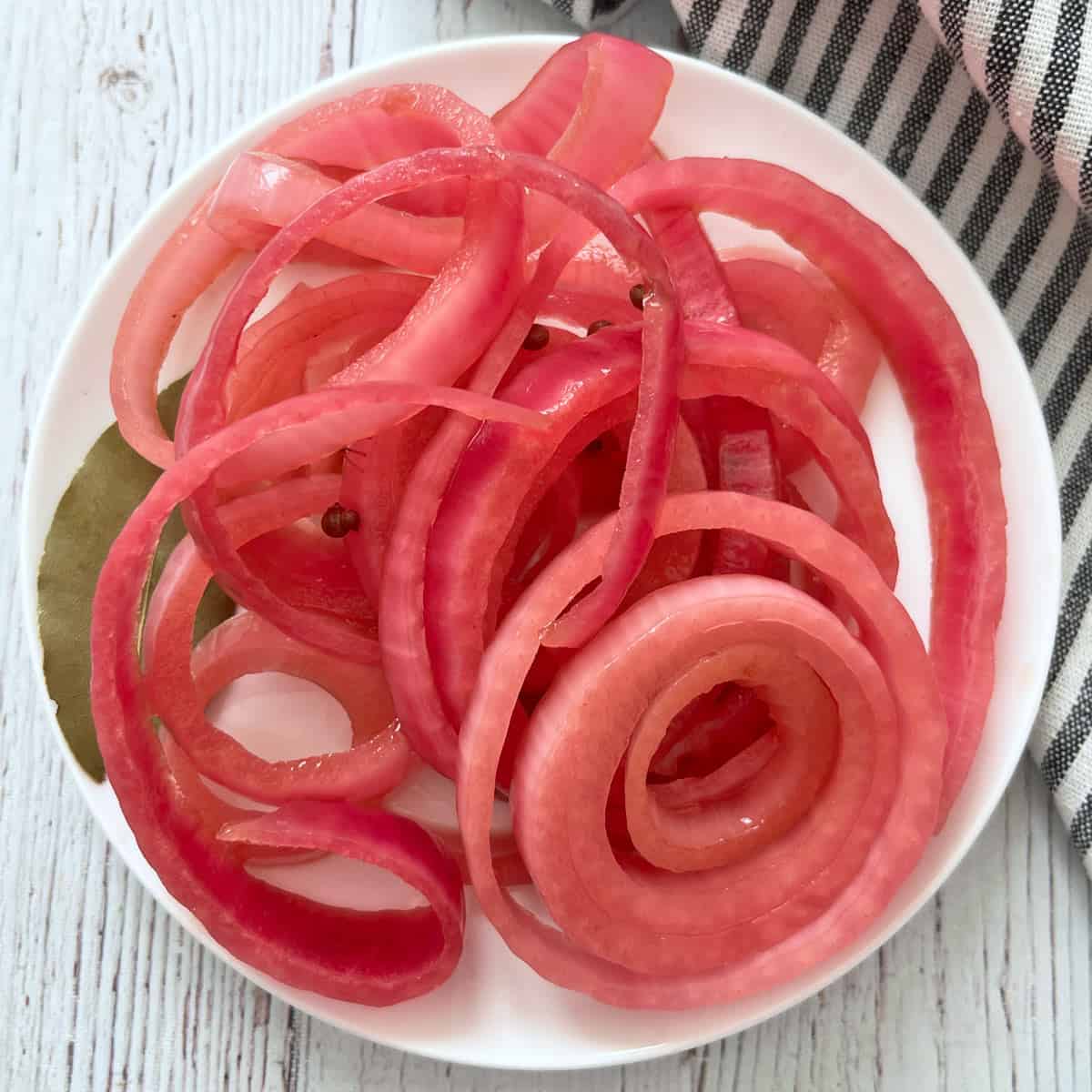 Red onions that were pickled with red wine vinegar are served on a white plate.