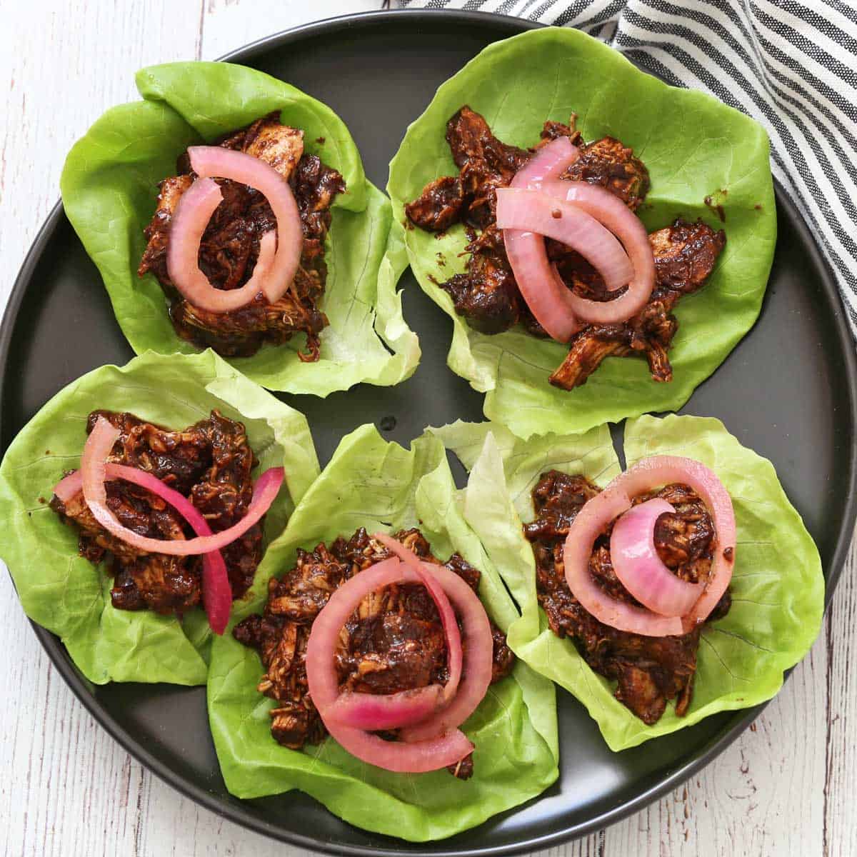 Pulled chicken is served in lettuce cups with pickled red onions.