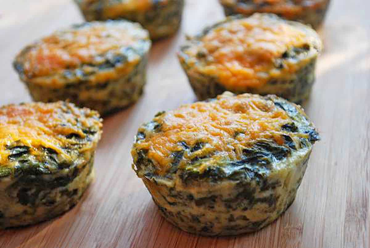Mini spinach quiches topped with shredded cheddar.