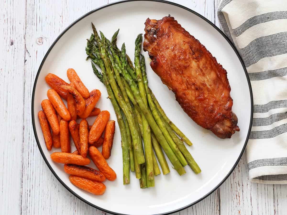 A turkey wing is served with roasted carrots and asparagus.