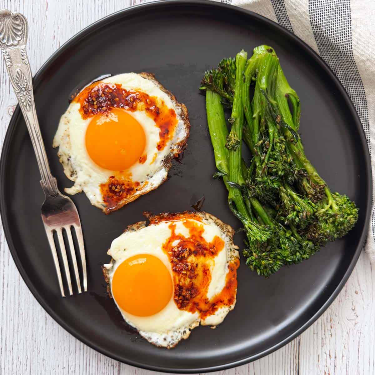 Fried eggs that were cooked in chili oil are served with broccolini.