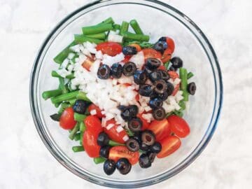 The veggies and olives were added to a bowl.