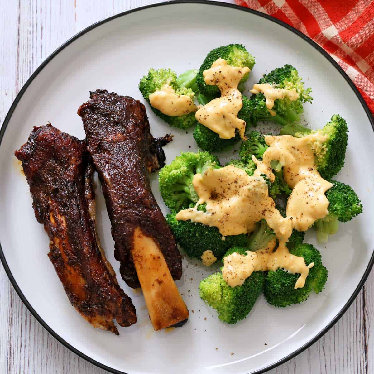 Beef back ribs are served with a side of microwave broccoli topped with cheese sauce.