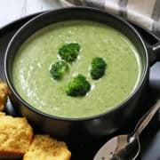 Broccoli soup is served in a dark bowl with cornbread muffins and a spoon.