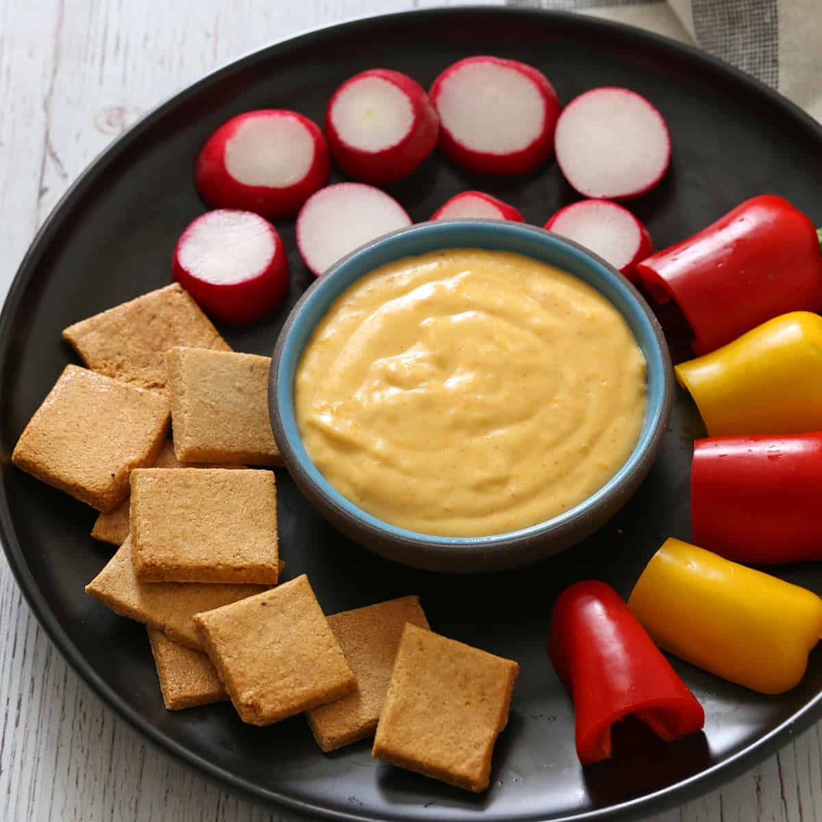 Cheese sauce is served with crackers, mini peppers, and radishes.
