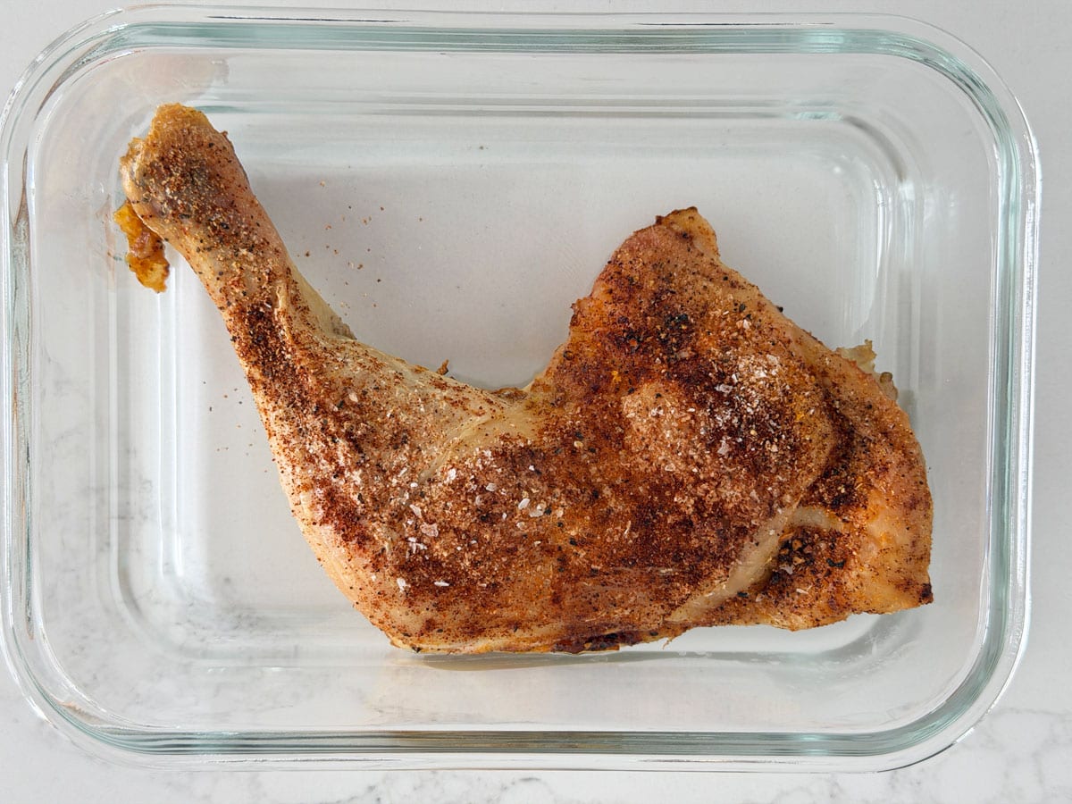 Chicken leg quarters leftovers in a glass container.