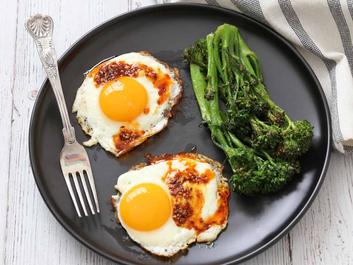 Grilled broccolini is served with fried eggs.