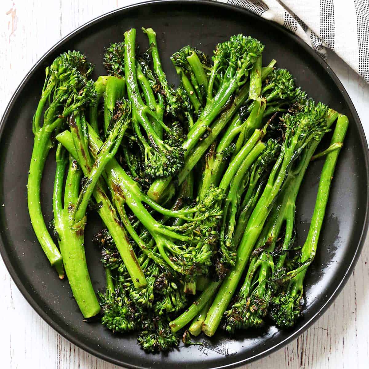 Grilled broccolini is served on a dark plate.