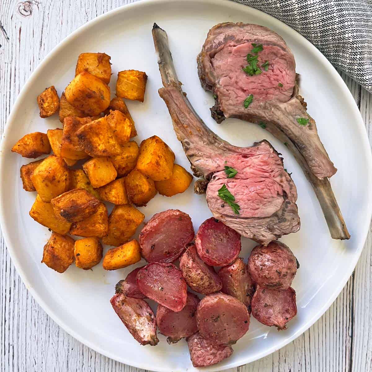 Roasted pumpkin, radishes, and lamb chops on a plate.