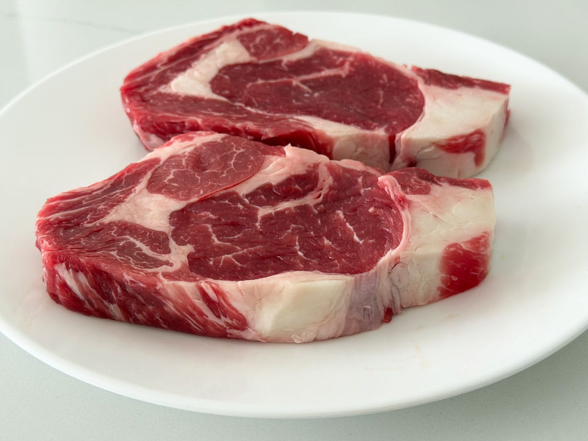 Two thinner raw ribeye steaks on a plate.