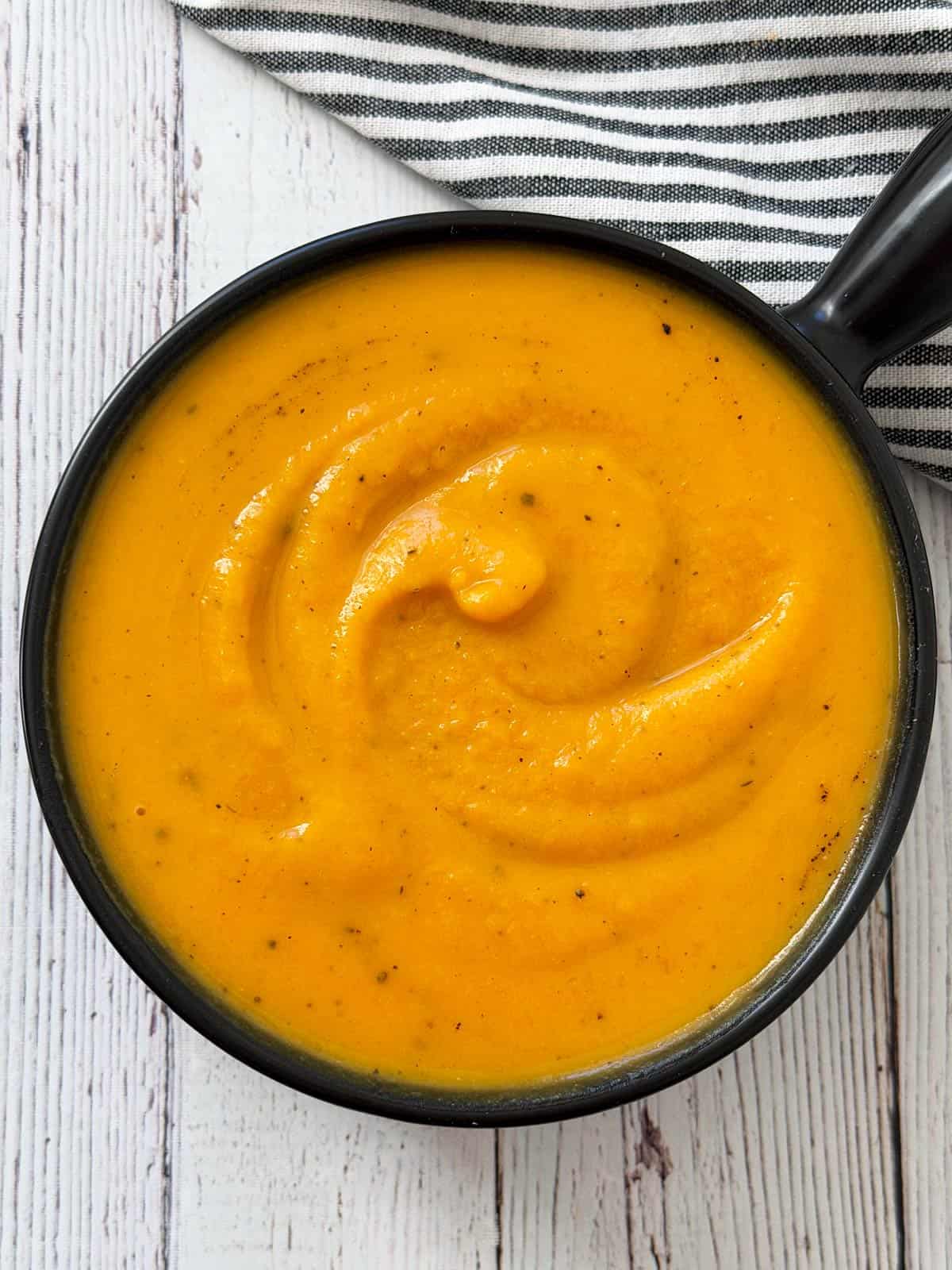 Butternut squash soup is served in a black bowl.