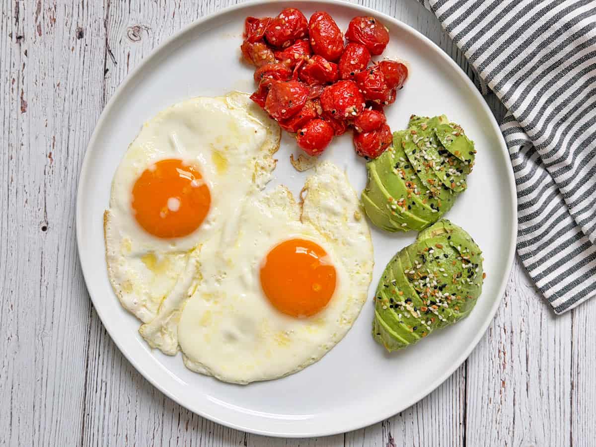 Roasted cherry tomatoes are served for breakfast with eggs and avocado.