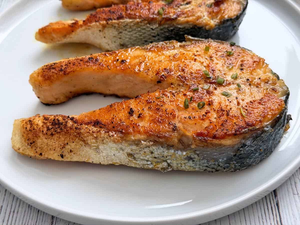 Two salmon steaks are served on a white plate.