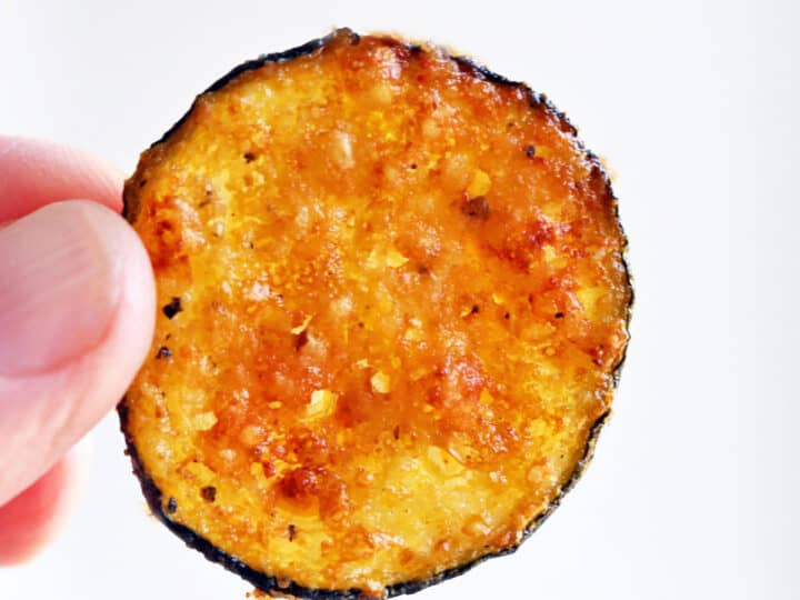A zucchini chip is held in the air.