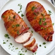 Bacon wrapped chicken breast is served on a plate, topped with parsley.
