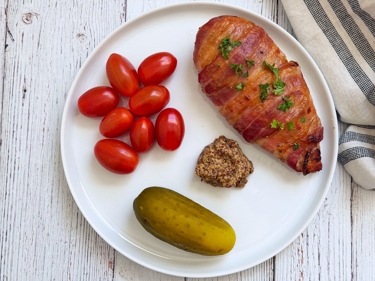 Bacon wrapped chicken leftovers are served with tomatoes, pickles, and mustard.